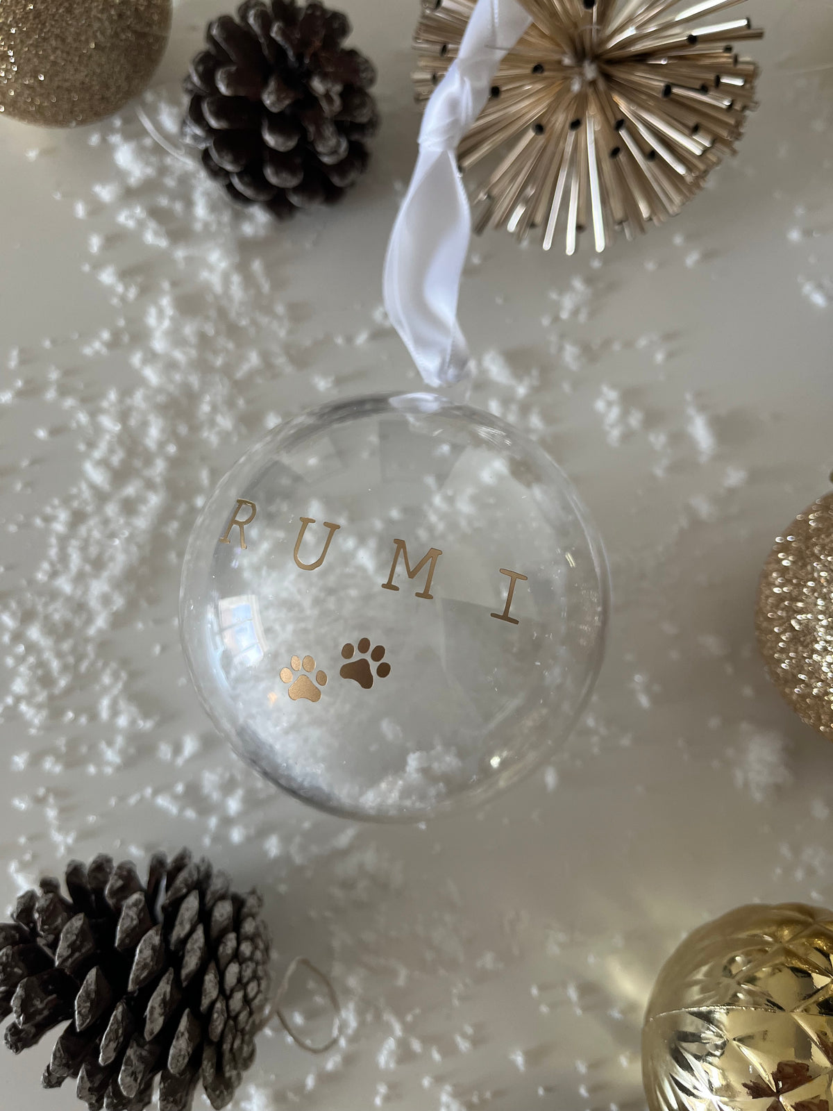 Clear glass ornament with 'RUMI' branding surrounded by decorative items on a light background