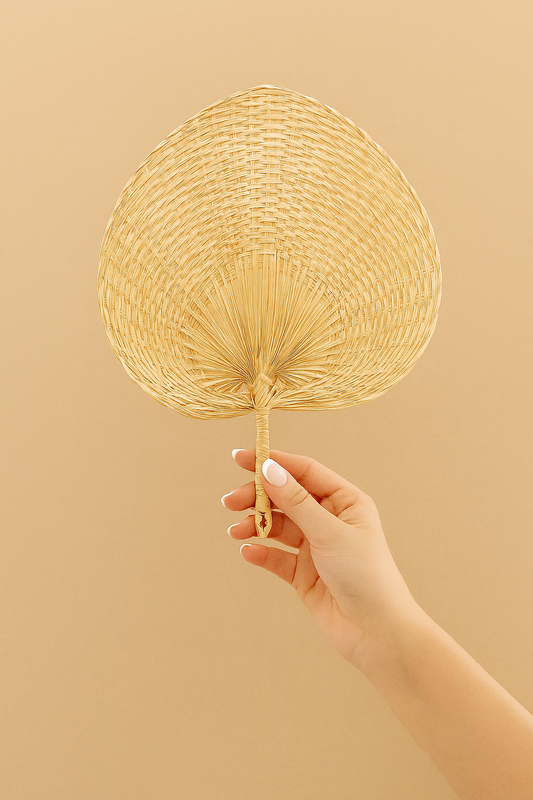 Hand holding a woven straw rattan fan against a beige background