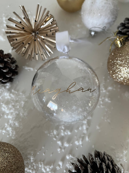 Clear glass ornament with text, surrounded by festive decorations on a white background.