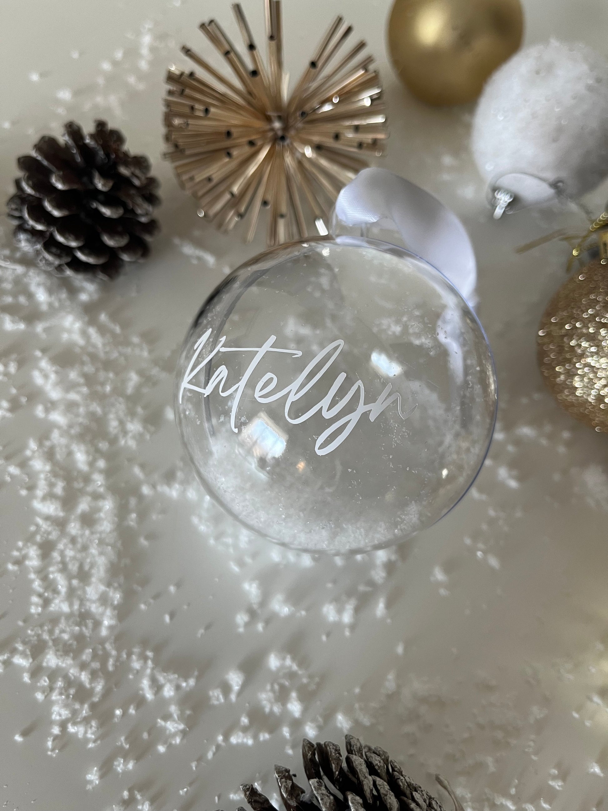 Clear glass ornament with 'Mistletoe' text, surrounded by Christmas decorations on a white background