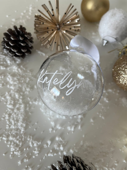 Clear glass ornament with 'Mistletoe' text, surrounded by Christmas decorations on a white background