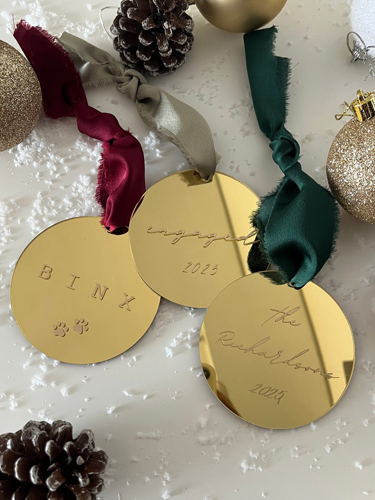 Gold Christmas tags with ribbons and pinecones on a textured surface
